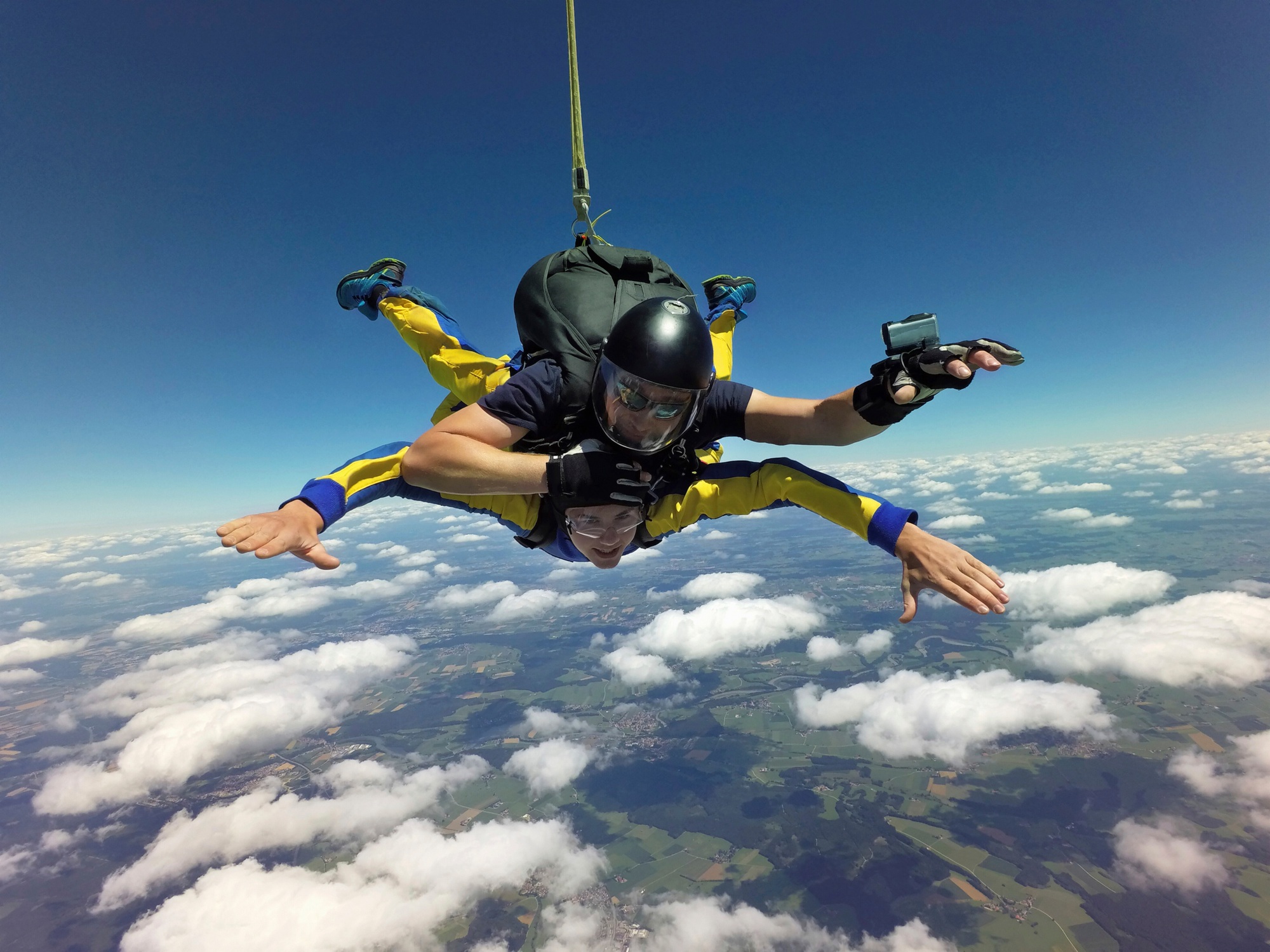 Portrait of tandem skydivers free falling above clouds and landscape