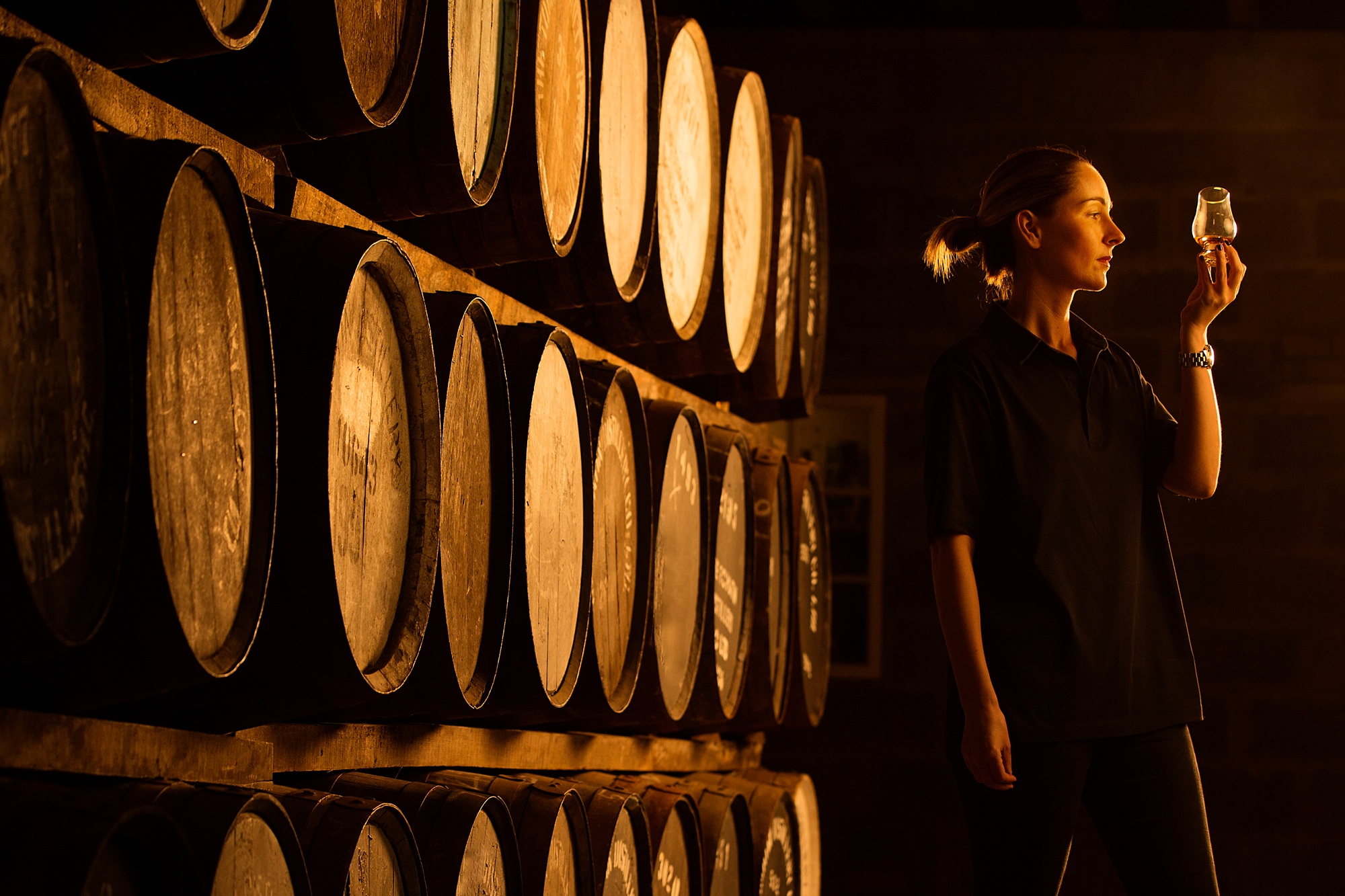 Female taster looking at the colour of whisky in glass at whisky distillery